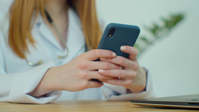 白大褂女医生使用现代智能手机触摸屏设备。医生使用手机向患者发送短信，告知医疗检查结果。