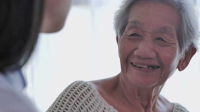 亚洲老年妇女听亚洲年轻女护士医生在咨询和手握她的年长女性病人在家。在家里照顾者