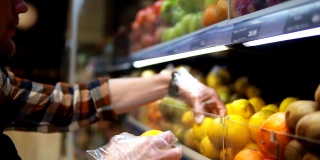 超市里，店员戴着透明手套，用各种各样的有机食品填满柠檬货架。超市店员正在把水果放在商店的货架上
