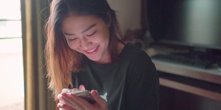 年轻的亚洲成年女性在家里使用智能手机。