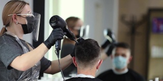 为预防新型冠状病毒感染症(Covid-19病毒)而采取安保措施的美发师，给戴着医用口罩的男子吹风，保持社交距离，在美容院用医用口罩、面罩和橡胶手套剪头发