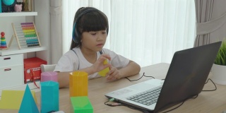 亚洲女学生视频会议e-learning几何形状与老师和同学在家里的客厅电脑上。在家教育和远程学习，在线，教育和互联网。