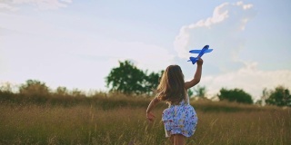 日落时分，美丽的小女孩和她的飞机玩具在草地上奔跑。慢动作