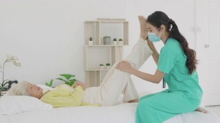 亚洲老年妇女在她的膝盖关节炎接受关节炎物理治疗康复专业护士或家庭健康助理在卧室在家。视频素材模板下载
