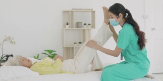 亚洲老年妇女在她的膝盖关节炎接受关节炎物理治疗康复专业护士或家庭健康助理在卧室在家。