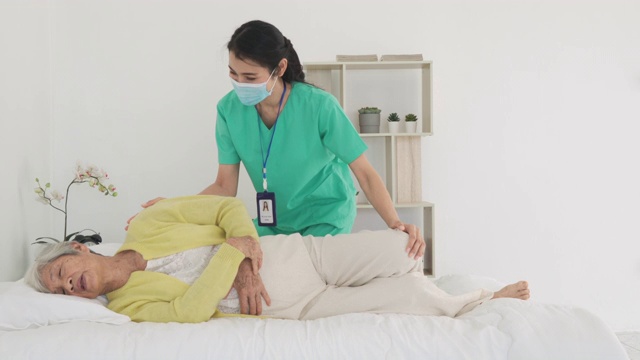 亚洲老年妇女在她的身体关节炎接受关节炎物理治疗康复专业护士或家庭健康助理在卧室在家。