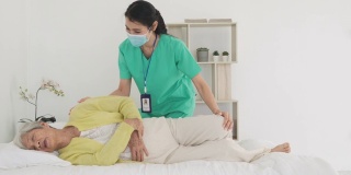 亚洲老年妇女在她的身体关节炎接受关节炎物理治疗康复专业护士或家庭健康助理在卧室在家。