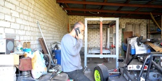 成年机械师站在车库或车间里打电话。使用电话与客户讨论汽车大师的简介。有人从事维修汽车。慢镜头