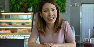 一名亚洲妇女在咖啡店的视频会议中对着摄像机说话