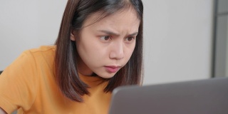 疲惫的年轻亚洲女性使用笔记本电脑，在长时间使用电脑工作后，在家庭办公室感觉眼睛疲劳。