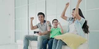 亚洲家庭的父亲和儿子一起在客厅玩电脑游戏与手机控制器，母亲是欢呼的玩家。