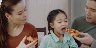 亚洲人喜欢在家吃美味的披萨。父母和女儿吃着外卖的美味意大利菜。概念食品外卖