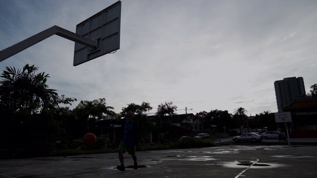 清晨，一名亚裔中国老人在篮球场上练习篮球，慢镜头中的剪影