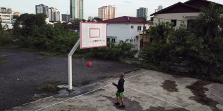 在无人机的镜头下，一名亚裔中国老人在篮球场练习篮球