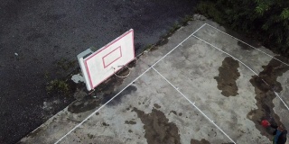 在无人机的镜头下，一名亚裔中国老人在篮球场练习篮球