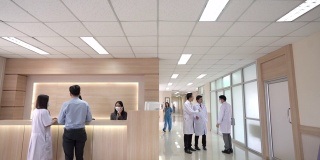 4K宽镜头的大堂等候区在现代化的医院或医疗设施，病人在询问柜台和一组专业医生和护士在医疗中心的卫生服务。