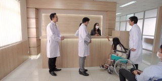 亚洲男医生在医院或医疗机构大堂向年轻女病人询问健康问题。一群医生帮助坐在轮椅上的生病妇女。医疗保健服务理念。