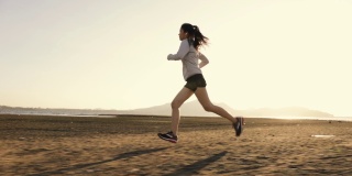 强壮年轻的亚洲女运动员跑步运动员速度跑训练锻炼在海滩上最后一个美丽的日落。医疗保健的生活方式的概念。