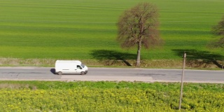 送货车。邮政递送服务。鸟瞰图拍摄汽车在空旷的乡村道路上行驶。在农村。卡车驶过美丽的郊区。鸟瞰春季农田。
