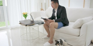 亚洲男子，上衣穿西装或职业装，下身穿运动裤或平角裤。商务视频会议使用笔记本电脑和平板电脑进行在线会议。在家工作和远程工作。