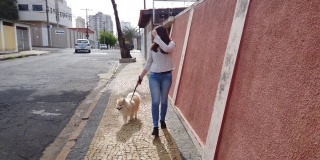 一名年轻女子带着她的狗走在街上，戴着防护口罩。