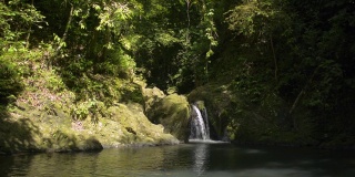 小瀑布流过群山。美丽的淡水在阳光下流入自然池塘在丛林。
