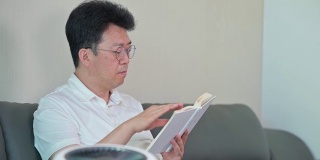 一位亚洲中年男子正在客厅里用空气净化器看书。