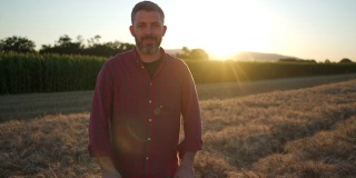 一个中年现代农民的肖像，站在麦田里双臂交叉在日落