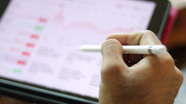 亚洲商人在咖啡店用平板电脑工作，查看股票趋势图和财务分析