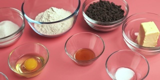 粉底玻璃碗中的巧克力饼干配料:红糖、白糖、巧克力片、鸡蛋、面粉、黄油、香草精、小苏打、4K盐。