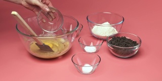 在粉色背景的玻璃碗中加入/混合巧克力片饼干配料:红糖、白糖、巧克力片、鸡蛋、面粉、黄油、香草精、小苏打、4K盐。