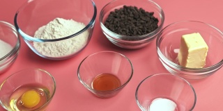 粉底玻璃碗中的巧克力饼干配料:红糖、白糖、巧克力片、鸡蛋、面粉、黄油、香草精、小苏打、4K盐。