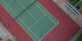 一个男孩和一个女孩正在做网球练习在硬地球场高清视频无人机的观点