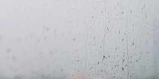 镜头选择焦点雨点与模糊的背景窗户，雨天，水滴玻璃，感觉孤独和悲伤的概念。坏天气的一天。看看窗外的景色，