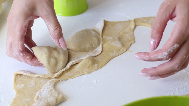 一个女人用玻璃杯包饺子。在面团中挤出所需形状。煮饺子。