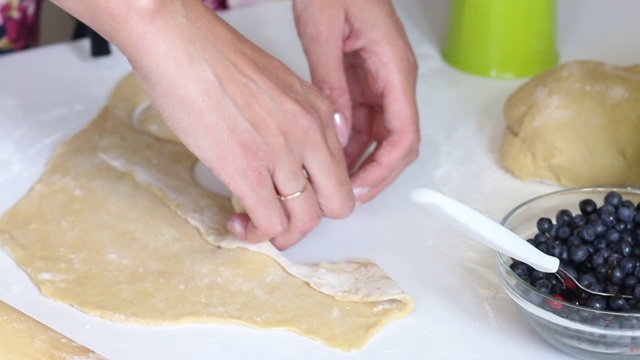 一个女人用玻璃杯包饺子。在面团中挤出所需形状。用蓝莓和樱桃做饺子。