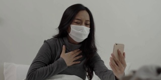 生病的年轻亚洲女子坐在床上用智能手机与医生进行在线视频通话。