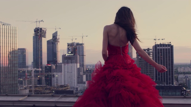 在屋顶上跳舞的解放女性。穿着红色的礼服欣赏城市全景
