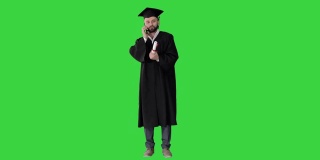 快乐毕业的年轻人戴着帽子和长袍在绿色屏幕上与父母聊天，色度键