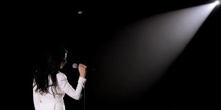 一个美丽的歌手在黑暗的舞台上在白色聚光灯下。