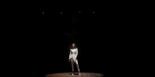 一个美丽的歌手在黑暗的舞台上在白色聚光灯下。