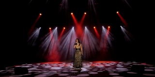 一个女孩在灯光闪烁的泛光灯下，在黑暗的舞台上唱歌