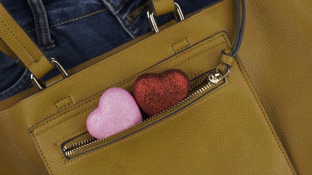 两颗心从一个女性黄色包的口袋里伸出来。旋转。爱情与时尚的背景。