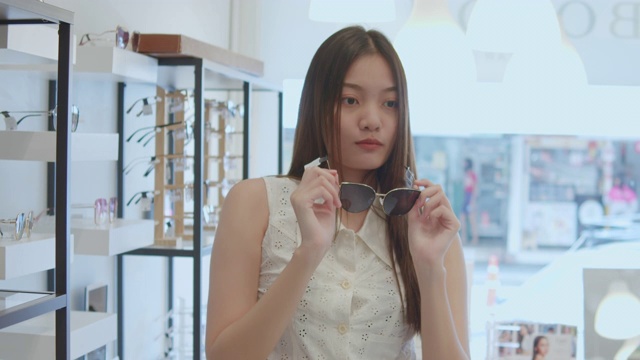 年轻的亚洲女人在光学商店挑选和试穿眼镜，慢镜头