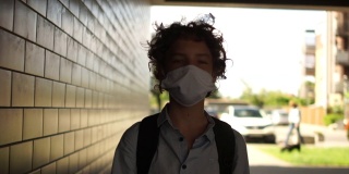 一个卷发戴面具的男孩沿着城市地下通道走着。回到学校，隔离后的生活