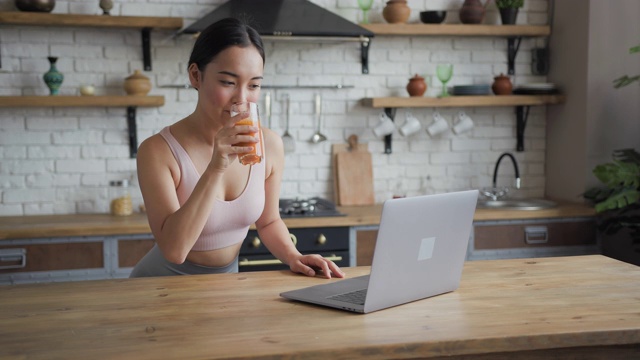 健康的亚洲女性使用笔记本电脑和喝橙汁