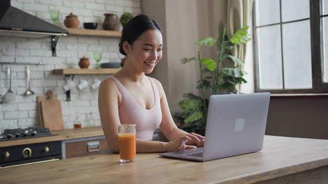 健康的亚洲女性使用笔记本电脑，发短信，喝橙汁和微笑