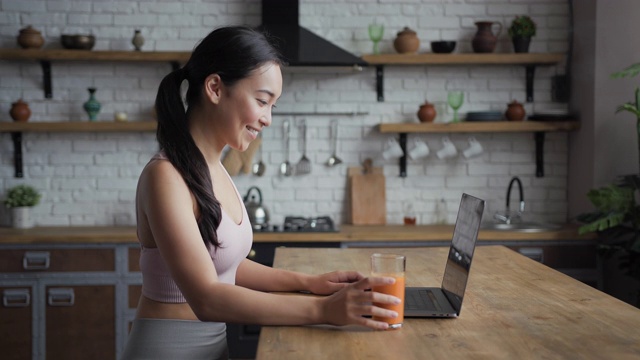 健康的亚洲女性用手提电脑，发短信，喝新鲜果汁，侧视图