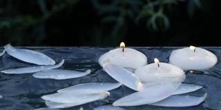 小蜡烛燃烧和荷花花瓣落入水中的特写