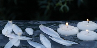 小蜡烛燃烧和荷花花瓣落入水中的特写